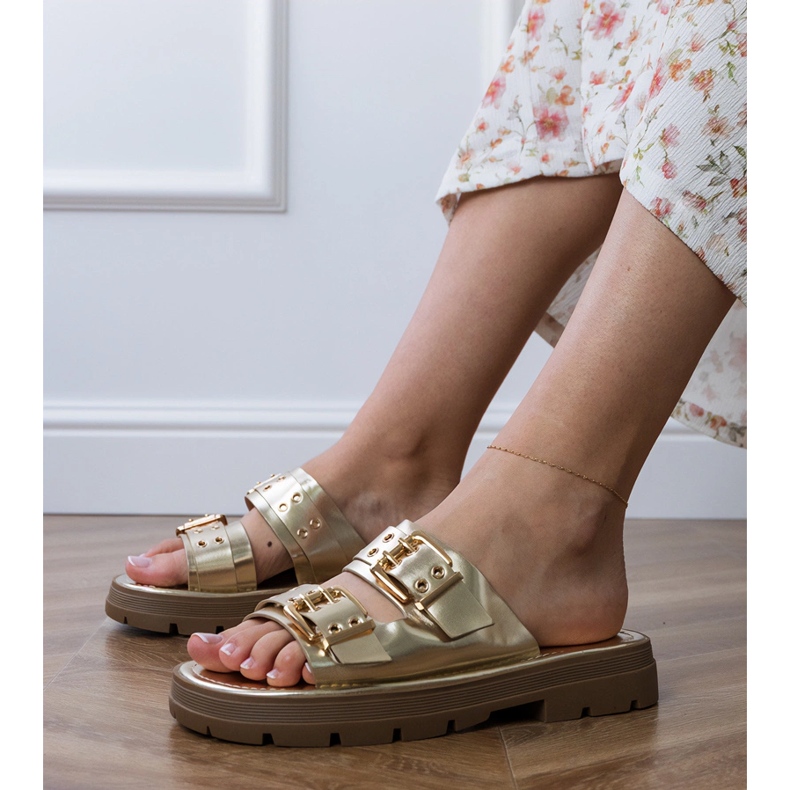 Les tongs plats dorés avec des pinces sur les rayures d'or