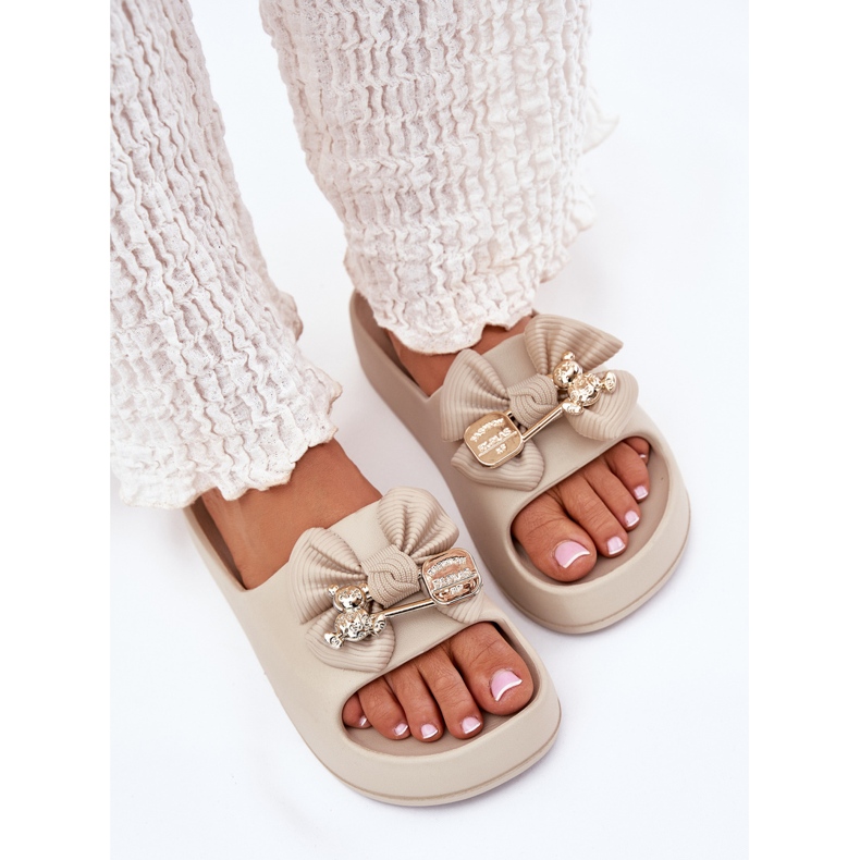 Les tongs de mousse pour femmes sur la plate-forme avec un arc et une broche beige noire